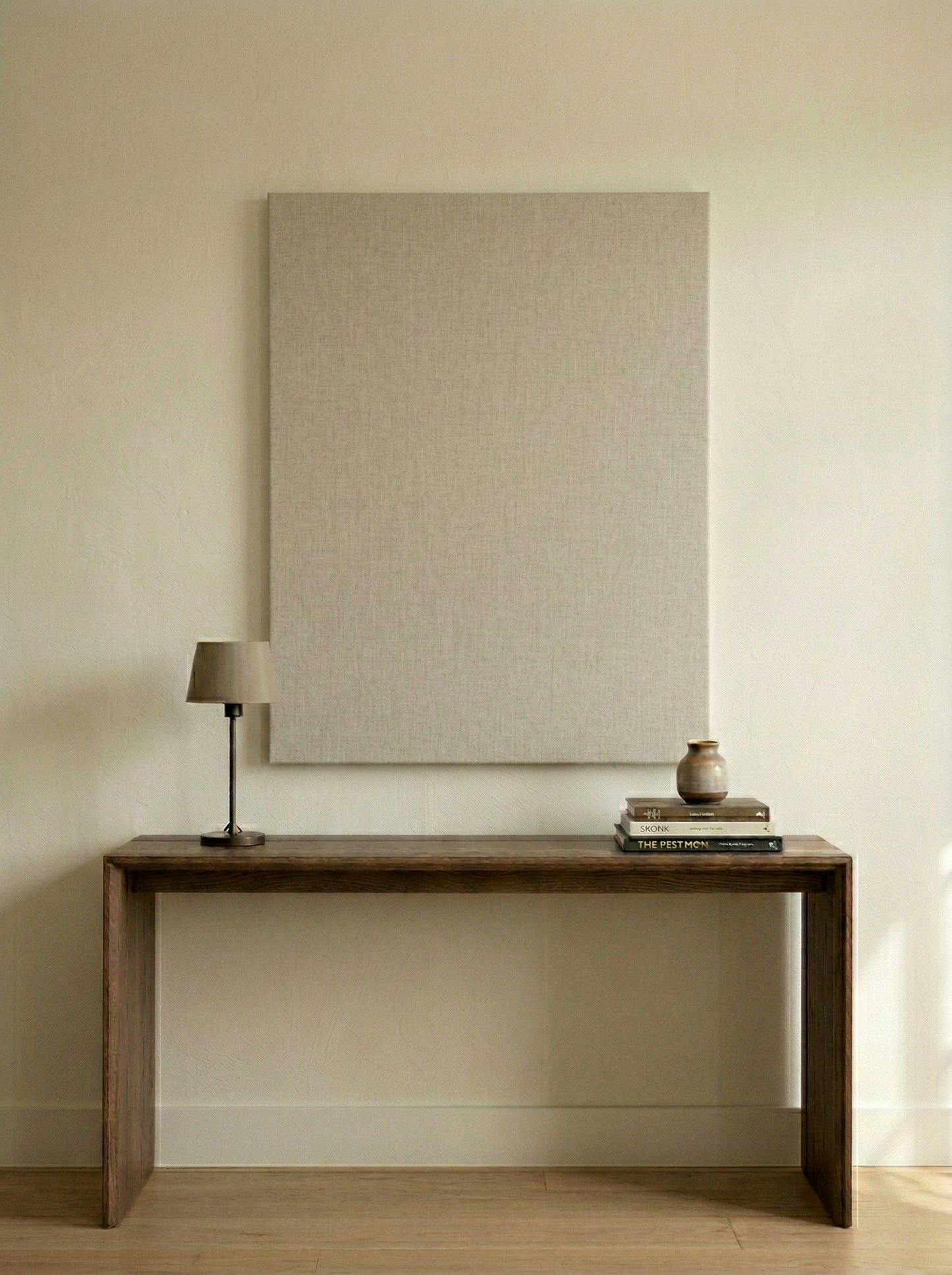 Wooden console table with a lamp and decorative items against a beige wall.